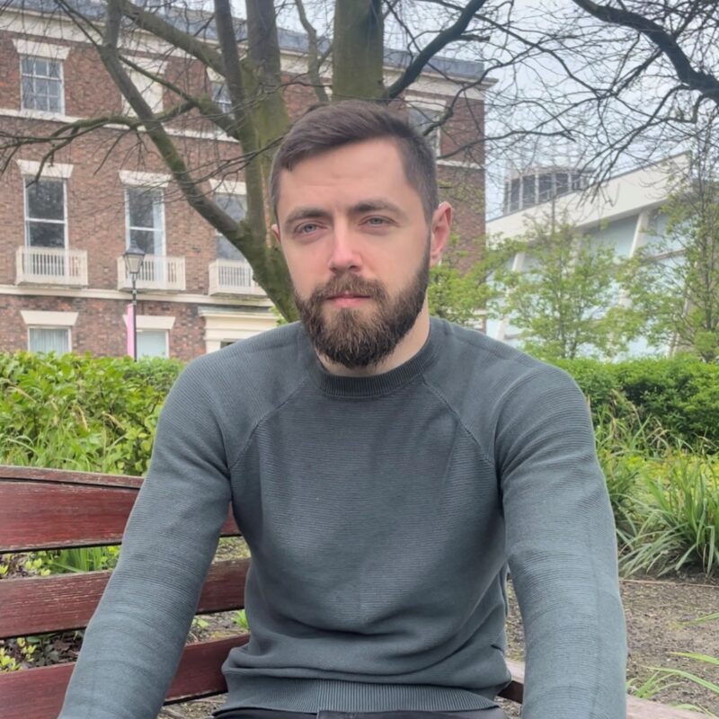 Photo of man with beard sat on a park bench