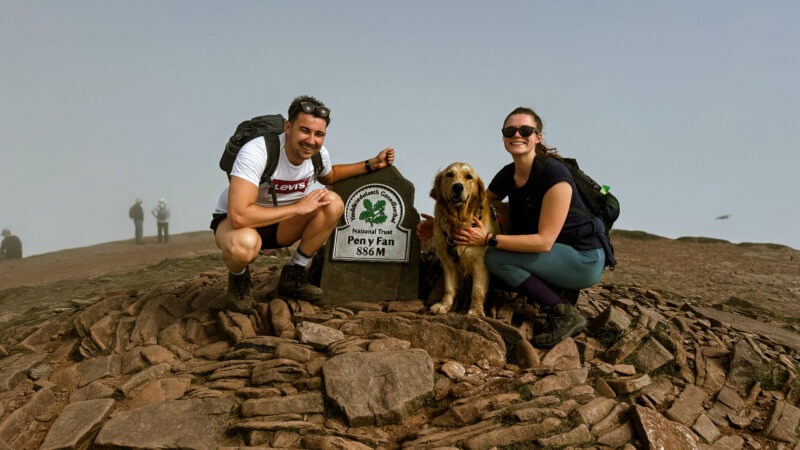 Man and a woman on top of a mountain with a dog