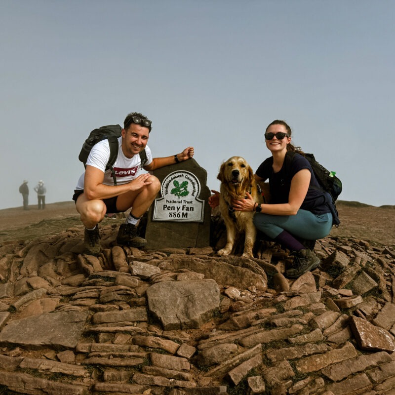 Man and a woman on top of a mountain with a dog